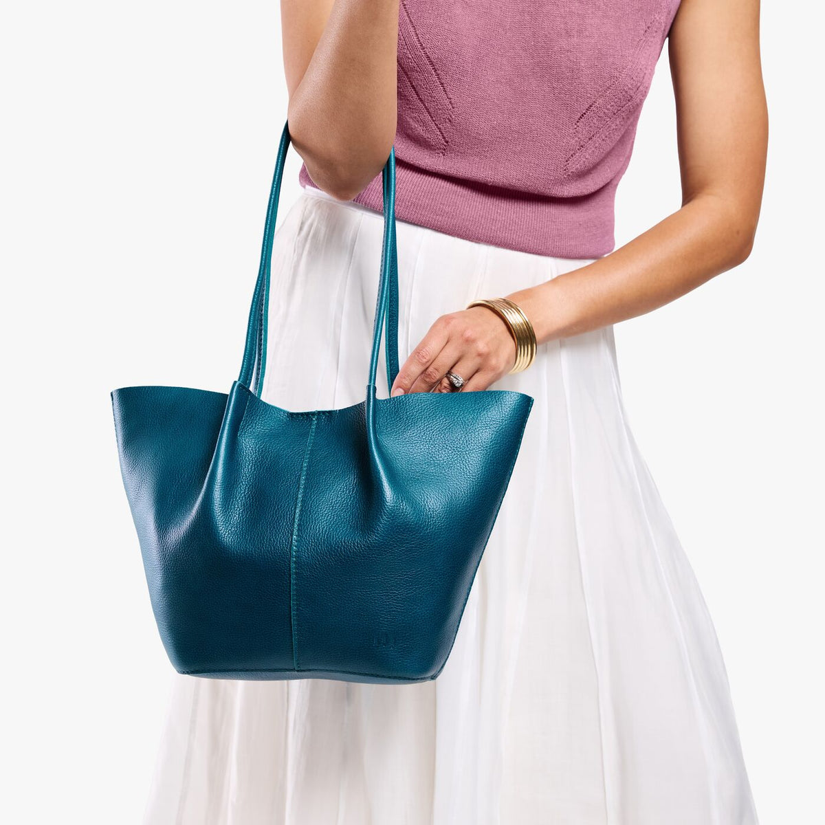 Model wearing mauve sleeveless top, white skirt, and gold wrist bangles carrying Large Devan Bucket Tote in Planetary