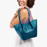 Model wearing mauve sleeveless top, white skirt, and gold wrist bangles carrying Large Devan Bucket Tote in Planetary