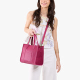 Cosmo | Model holding structured mid-size tote bag with overlapping panels and crossbody strap
