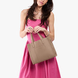 Stone | Model holding structured mid-size tote bag with overlapping panels and crossbody strap