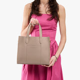 Stone | Model holding structured mid-size tote bag with overlapping panels and crossbody strap