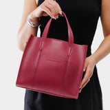 Berry Good | Model holding structured mid-size tote bag with overlapping panels and crossbody strap