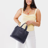 Night Owl | Model holding structured mid-size tote bag with overlapping panels and crossbody strap