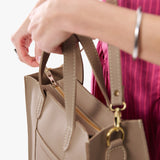 Stone Zipper | Model holding structured mid-size tote bag with overlapping panels and crossbody strap