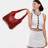 Chili Red Large | A model holding a u-shaped, flat-bottomed leather shoulder bag with two outside pockets