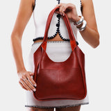 Chili Red Large | A model holding a u-shaped, flat-bottomed leather shoulder bag with two outside pockets