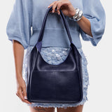 Cobalt Large | A model holding a u-shaped, flat-bottomed leather shoulder bag with two outside pockets