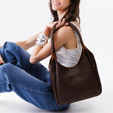 Coldbrew Large | A model holding a u-shaped, flat-bottomed leather shoulder bag with two outside pockets