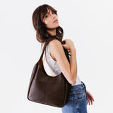 Coldbrew Large | A model holding a u-shaped, flat-bottomed leather shoulder bag with two outside pockets