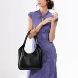 Pebbled--Black Large | A model holding a u-shaped, flat-bottomed leather shoulder bag with two outside pockets