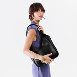 Pebbled--Black Large | A model holding a u-shaped, flat-bottomed leather shoulder bag with two outside pockets