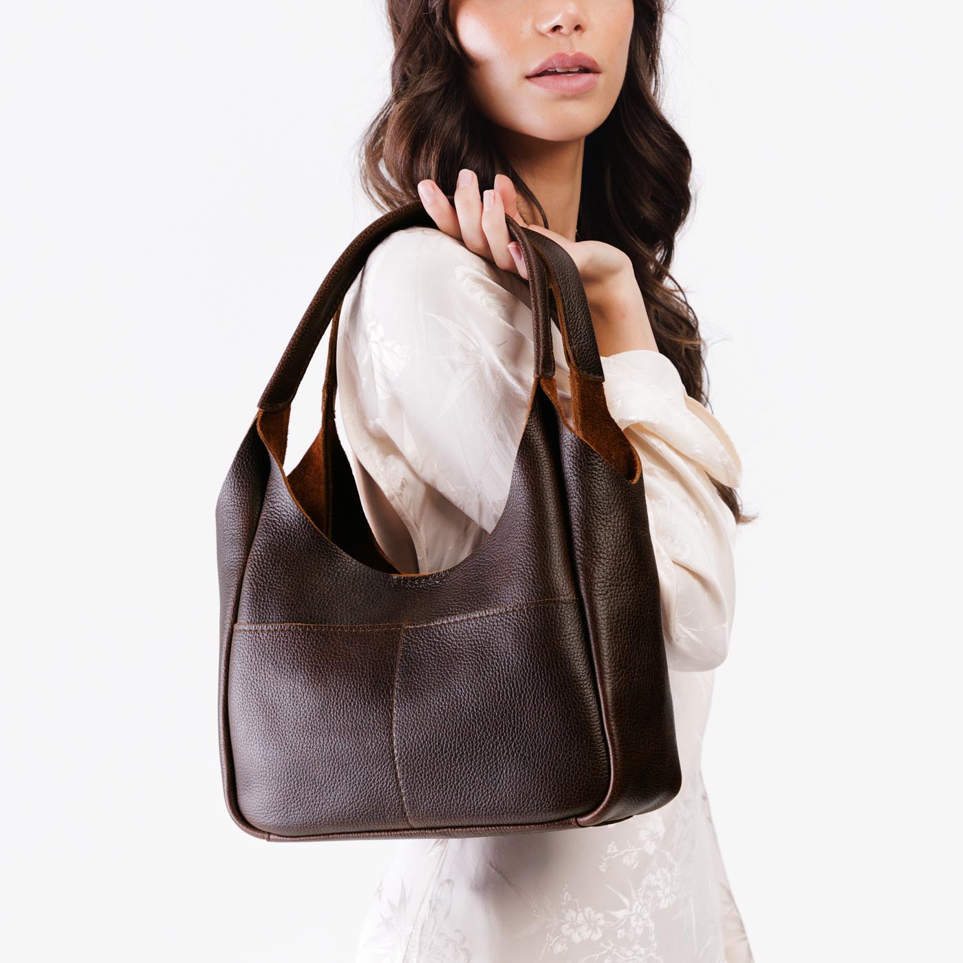 Coldbrew*Medium | A model holding a u-shaped, flat-bottomed leather shoulder bag with two outside pockets