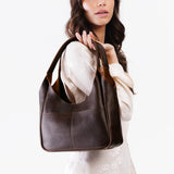 Coldbrew Medium | A model holding a u-shaped, flat-bottomed leather shoulder bag with two outside pockets