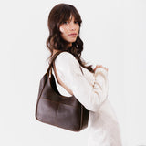Coldbrew Medium | A model holding a u-shaped, flat-bottomed leather shoulder bag with two outside pockets