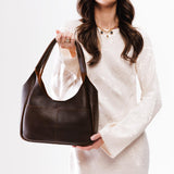 Coldbrew Medium | A model holding a u-shaped, flat-bottomed leather shoulder bag with two outside pockets