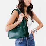 Forest Green Medium | A model holding a u-shaped, flat-bottomed leather shoulder bag with two outside pockets