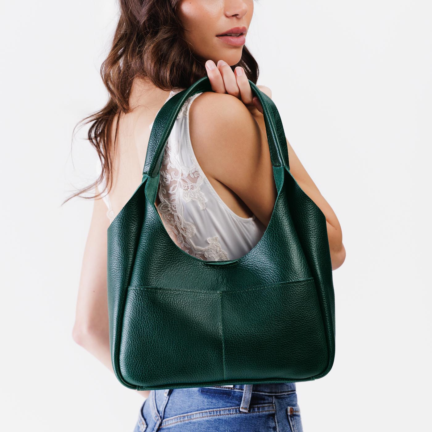Forest Green*Medium | A model holding a u-shaped, flat-bottomed leather shoulder bag with two outside pockets