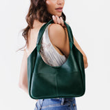 Forest Green Medium | A model holding a u-shaped, flat-bottomed leather shoulder bag with two outside pockets