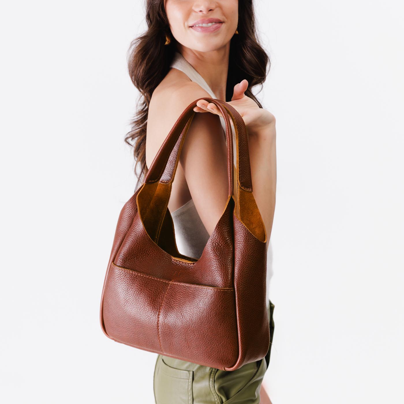Nutmeg*Medium | A model holding a u-shaped, flat-bottomed leather shoulder bag with two outside pockets