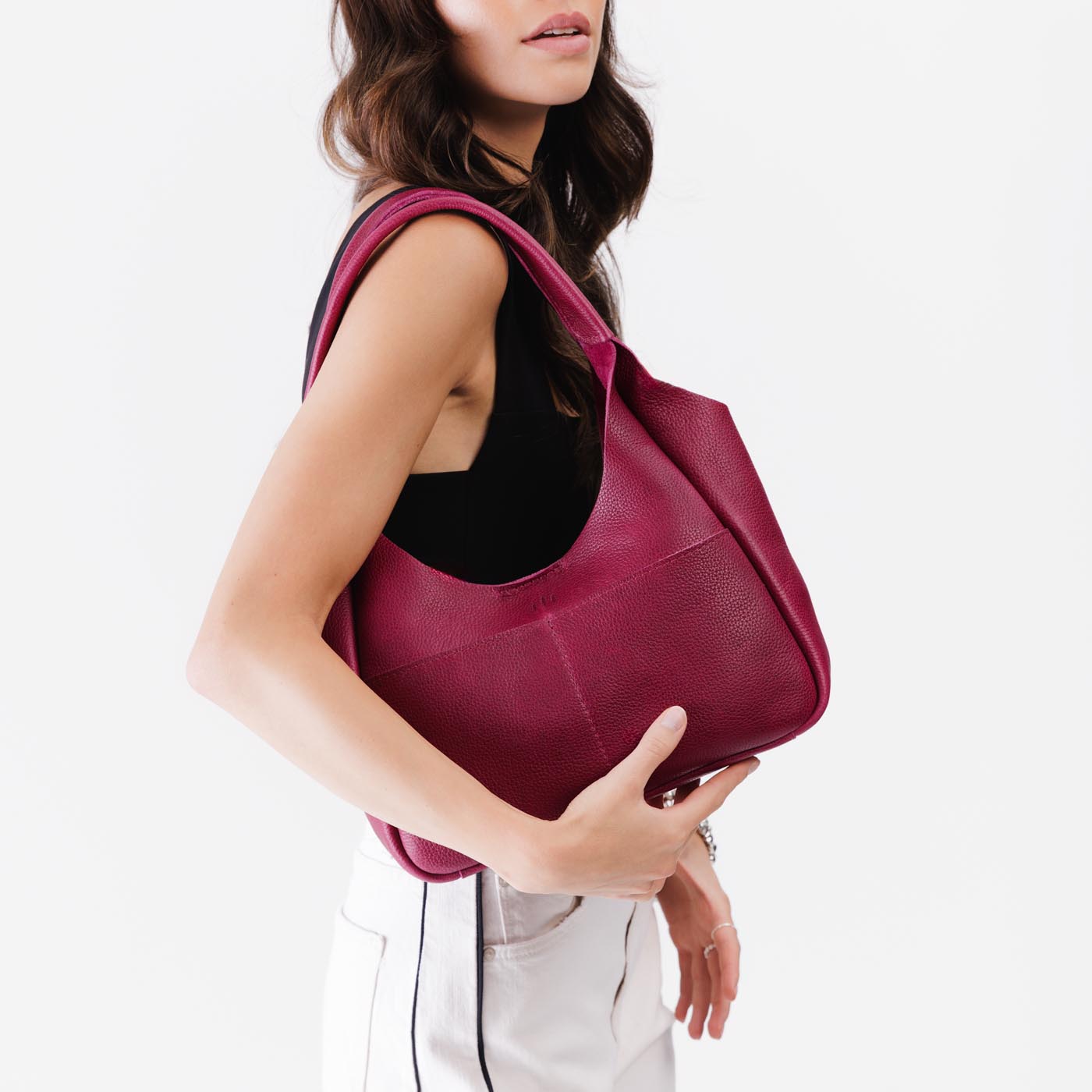 Orchid*Medium | A model holding a u-shaped, flat-bottomed leather shoulder bag with two outside pockets