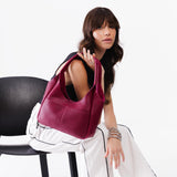 Orchid Medium | A model holding a u-shaped, flat-bottomed leather shoulder bag with two outside pockets