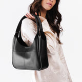 Pebbled--Black Medium | A model holding a u-shaped, flat-bottomed leather shoulder bag with two outside pockets