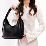 Pebbled--Black Medium | A model holding a u-shaped, flat-bottomed leather shoulder bag with two outside pockets