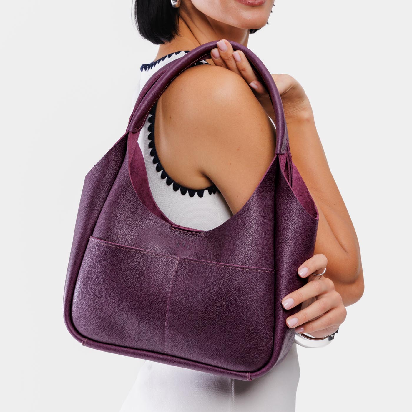 Plum*Medium | A model holding a u-shaped, flat-bottomed leather shoulder bag with two outside pockets