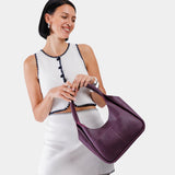 Plum Medium | A model holding a u-shaped, flat-bottomed leather shoulder bag with two outside pockets