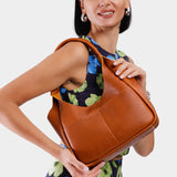 Sienna Medium | A model holding a u-shaped, flat-bottomed leather shoulder bag with two outside pockets