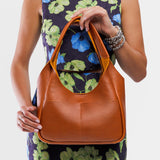 Sienna Medium | A model holding a u-shaped, flat-bottomed leather shoulder bag with two outside pockets