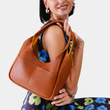 Sienna Medium | A model holding a u-shaped, flat-bottomed leather shoulder bag with two outside pockets