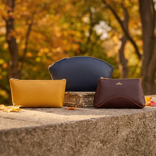 Three leather pouches are arranged on a stone ledge outdoors with a blurred autumn park background.