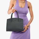 Black Medium | Model carrying leather tote bag with handles, adjustable crossbody strap, and two back pockets