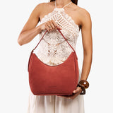 Cinnabar Medium | Model holding u-shaped, flat-bottomed leather shoulder bag with adjustable strap