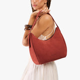 Cinnabar Medium | Model holding u-shaped, flat-bottomed leather shoulder bag with adjustable strap