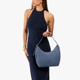 Denim Medium | Model holding u-shaped, flat-bottomed leather shoulder bag with adjustable strap