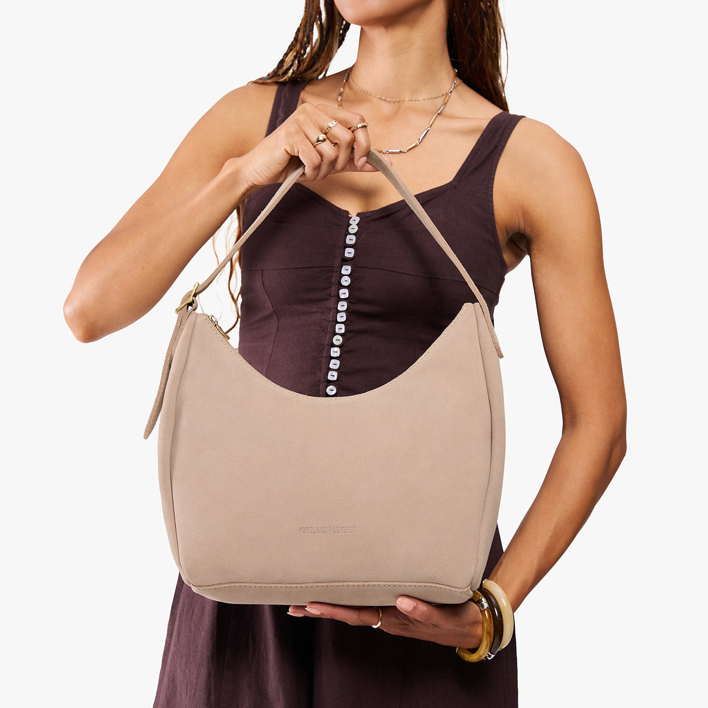 Taupe*Medium | Model holding u-shaped, flat-bottomed leather shoulder bag with adjustable strap