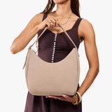 Taupe Medium | Model holding u-shaped, flat-bottomed leather shoulder bag with adjustable strap