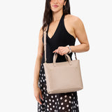 Oatmilk Zipper | Model holding midsize crossbody tote with handles, zipper top, and a pocket