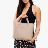 Oatmilk Zipper | Model holding midsize crossbody tote with handles, zipper top, and a pocket