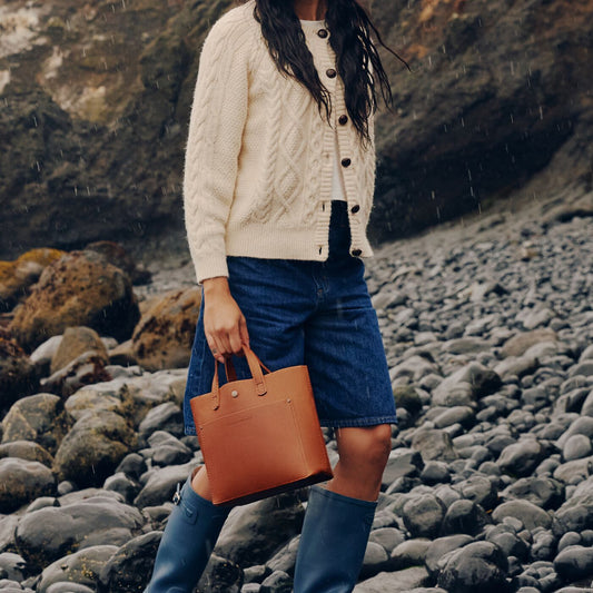 A model walkingon a rocky shore holding a Honey Mini Crossbody Bag.