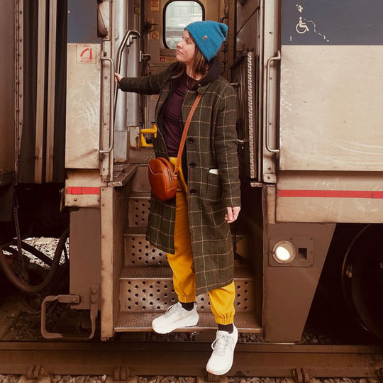 Person boarding a train wearing a long coat and brown crossbody bag