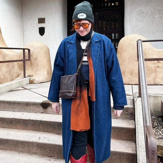 Person wearing a blue coat and brown crossbody bag standing on steps with a building in the background
