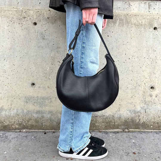Person holding a black leather handbag against a concrete wall