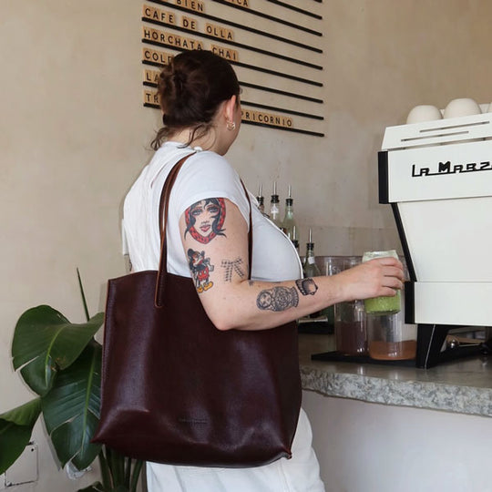 Person with tattoos wearing a brown leather bag in a coffee shop