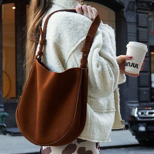 Person holding a brown leather bag and a coffee cup on a city street