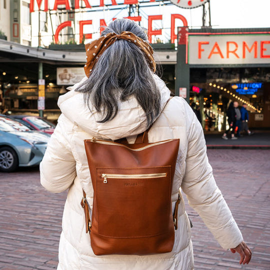 Person wearing a white coat and brown leather backpack in an urban setting with signs in the background