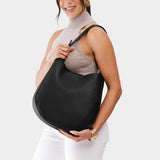 Pebbled--black Large | Woman wearing rounded shoulder bag with adjustable strap on a white background