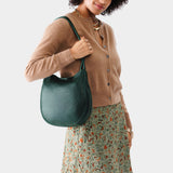 Forest Green Medium | Woman wearing rounded shoulder bag with adjustable strap on a white background